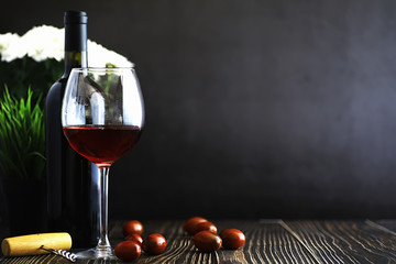 A glass of red dry wine on the table. Dark bottle and glass of wine.
