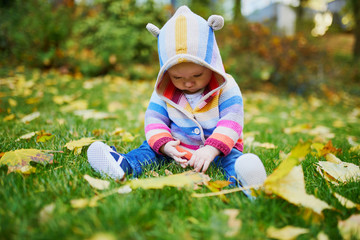Girl sitting on the grass and playing with colorful autumn leaves