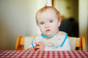 Cute baby girl eating carrot in the kitchen