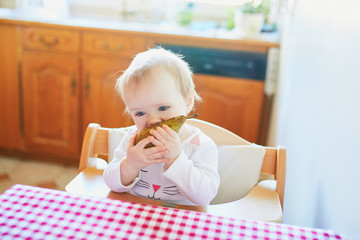 Fototapeta premium Cute baby girl eating pear in the kitchen