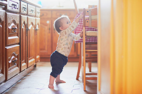Baby girl standing on the floor in the kitchen and holding on to furniture