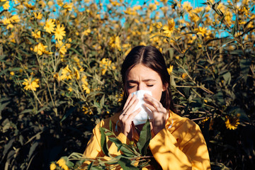 Woman is blowing her nose near flowers in bloom. Young girl sneezing and holding paper tissue in...