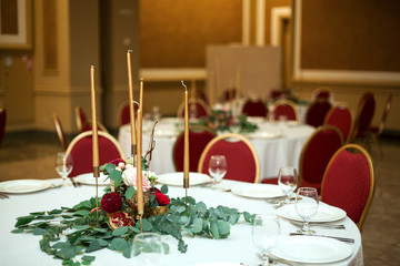 Festively decorated round banquet table in the restaurant. Fresh flowers are golden candles and red chairs. expensively rich