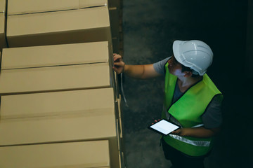 Top view of young warehouse worker man with safety hard hat is checking order details with a digital tablet at inventory room