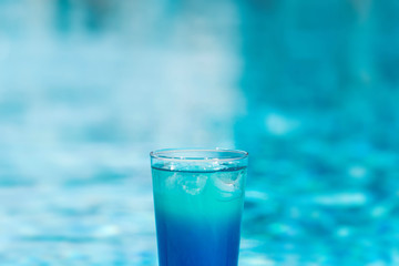 Blue coctail with ice in the glass on the swimming pool background. Resort tropical hotel in summer day and fresh water. Blurred backgraund with copy space.