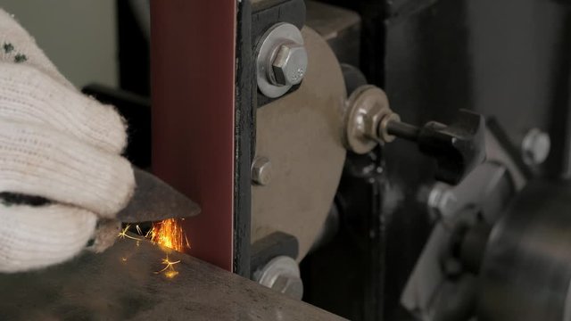 Grinder. Belt grinding machine. Metalworking machine. Grinder. Man sharpens the detail. Workshop. Sparks.