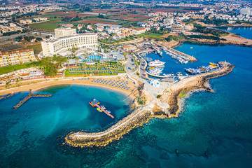 Cyprus. Protaras. The Paralimni harbour. Pernera. Kalamies beach top view. The jutting out into the sea beach forms the bays. St. Nicolas church Cyprus. Beach resort of Cyprus. Panorama with drone. - obrazy, fototapety, plakaty