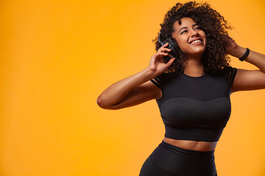 Lifestyle Concept. Portrait of beautiful African American woman with curly hair joyful listening to music on mobile phone. Yellow studio background. Copy Space.