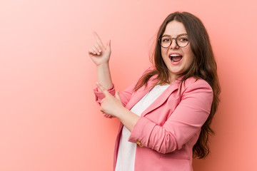 Young plus size business caucasian woman pointing with forefingers to a copy space, expressing excitement and desire.