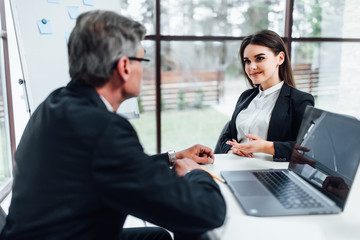 Older boss listening young manager woman in office, they are working with notebook.