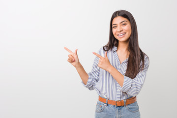 Young pretty arab woman pointing with forefingers to a copy space, expressing excitement and desire.
