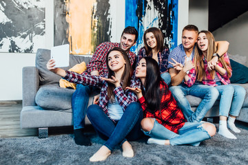 Group of funny young  friends sitting at home on sofa and making selfie together..