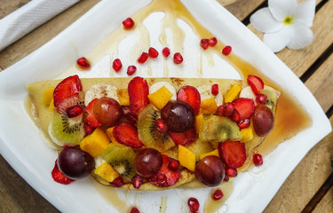 Delicious fruit pancake with maple syrup and cinnamon, tasty breakfast, cup of cappuccino