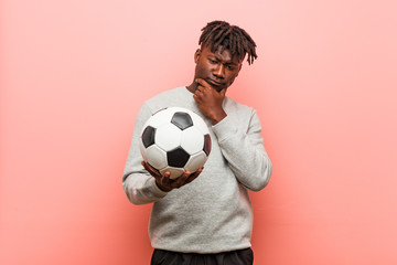 Young fitness black man holding a soccer ball looking sideways with doubtful and skeptical...