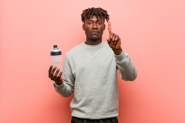 Young fitness black man holding a water bottle showing number one with finger.