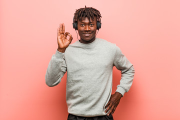 Young rasta black man listening to music with headphones cheerful and confident showing ok gesture.
