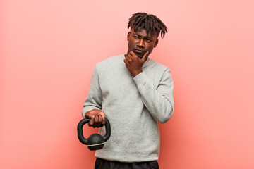 Young fitness black man holding a dumbbell looking sideways with doubtful and skeptical expression.