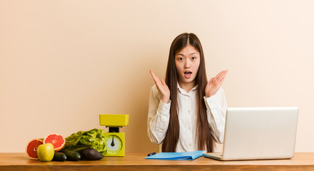 Obraz na płótnie Canvas Young nutritionist chinese woman working with her laptop surprised and shocked.