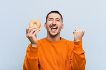Young caucasian man holding a donut cheering carefree and excited. Victory concept.