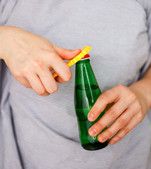 Woman in a light color t-shirt opens a green bottle of fizzy drink with a yellow opener