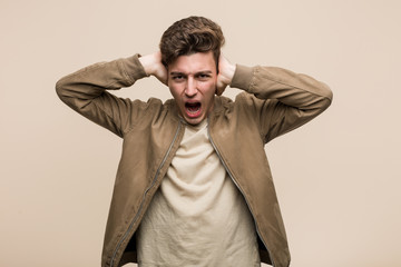 Young caucasian man wearing a brown jacket covering ears with hands trying not to hear too loud sound.