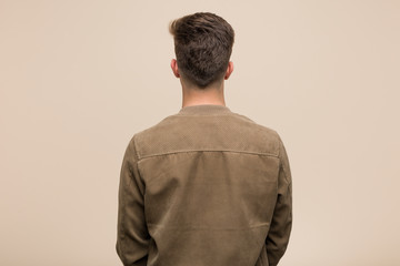 Young caucasian man wearing a brown jacket from behind, looking back.
