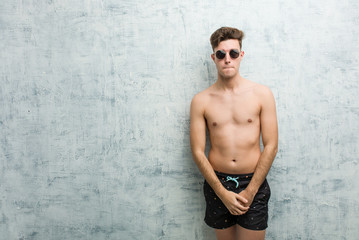 Young caucasian man wearing swimsuit confused, feels doubtful and unsure.