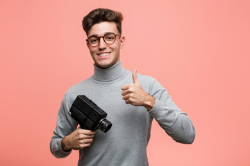 Young intellectual man holding a film camera smiling and raising thumb up