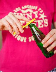 Woman in a bright t-shirt opens a green bottle of fizzy drink with a yellow opener