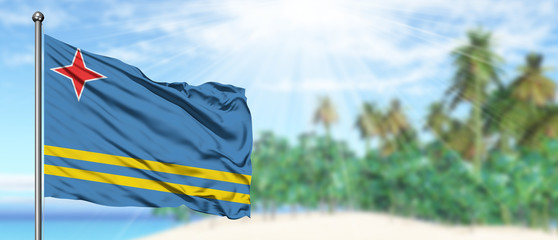 Waving Aruba flag in the sunny blue sky with summer beach background. Vacation theme, holiday concept.