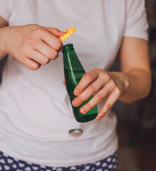 Woman in a light color t-shirt opens a green bottle of fizzy drink with a yellow opener