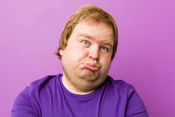 Fototapeta premium Young authentic redhead fat man blows cheeks, has tired expression. Facial expression concept.