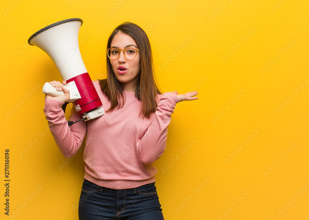 Wall mural Young cute woman holding a megaphone holding something on palm hand