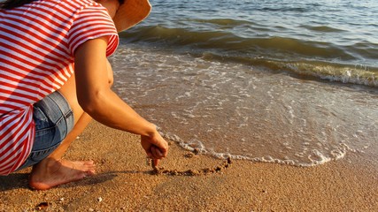 The girl sat on the beach by the sea and painted the heart on the sand