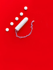 Tampon and female pain pills during menstruation on a red background. Protection from unwanted pregnancy, ovulation
