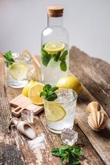 Bottle and two glasses of fresh lemonade with lemon slices, mint and ice on old wooden planks