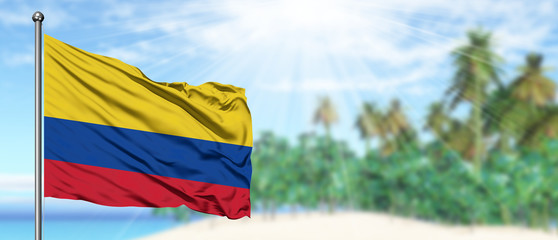 Waving Colombia flag in the sunny blue sky with summer beach background. Vacation theme, holiday concept.