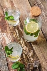 Bottle and two glasses of fresh lemonade with lemon slices, mint and ice on old wooden planks