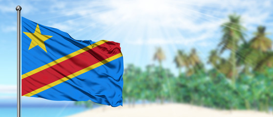 Waving Congo flag in the sunny blue sky with summer beach background. Vacation theme, holiday concept.