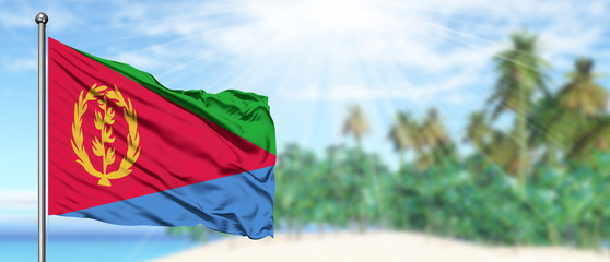 Waving Eritrea flag in the sunny blue sky with summer beach background. Vacation theme, holiday concept.