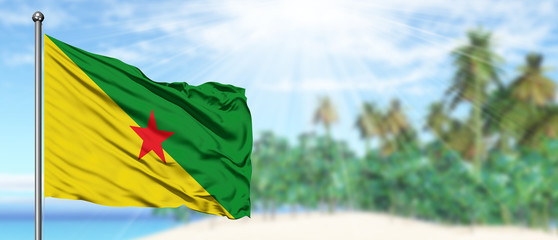 Waving French Guiana flag in the sunny blue sky with summer beach background. Vacation theme, holiday concept.