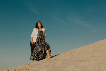 Outdoor fashion portrait of plus size woman wearing trendy animal print. Attractive curvy woman on the background of the desert and blue sky. Stylish accessories, summer dress, bag and jacket