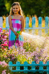 Playfull girl watering flowers with rain in the garden at summer day. Child using garden hose on...