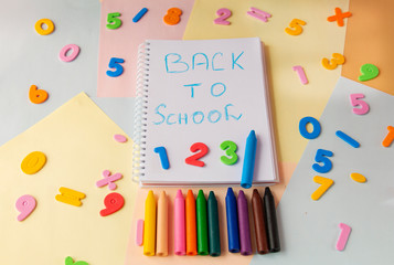 Back to school inscription in blue in a notebook, numbers and pencils on a colorful background top view