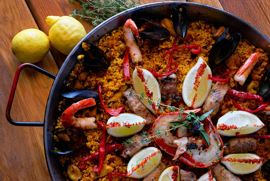 Delicious Spanish seafood paella, view from above. Cooked with sturgeon halibut fillet, peeled shrimps squids, mussels lobster decorated with lemon tomato red bell pepper in pan, close up image .