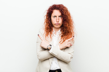Young natural redhead business woman isolated against white background points sideways, is trying to choose between two options.