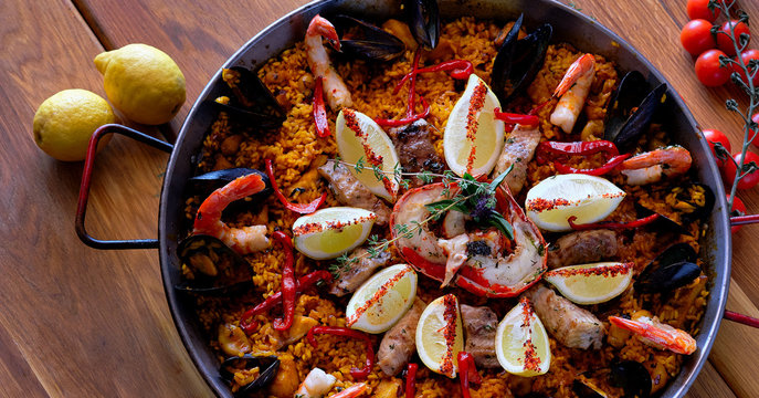 Delicious Spanish seafood paella, view from top. Cooked with sturgeon halibut fillet, peeled shrimps squids, mussels and lobster decorated with lemon slices red bell pepper in a pan, close up image .
