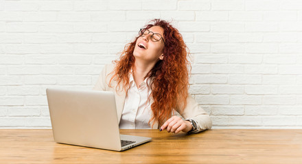 Young redhead curly woman working with her laptop relaxed and happy laughing, neck stretched showing teeth.