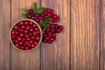 cowberries with leaves and wooden cup on wooden background