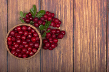 cowberries with leaves and wooden cup on wooden background